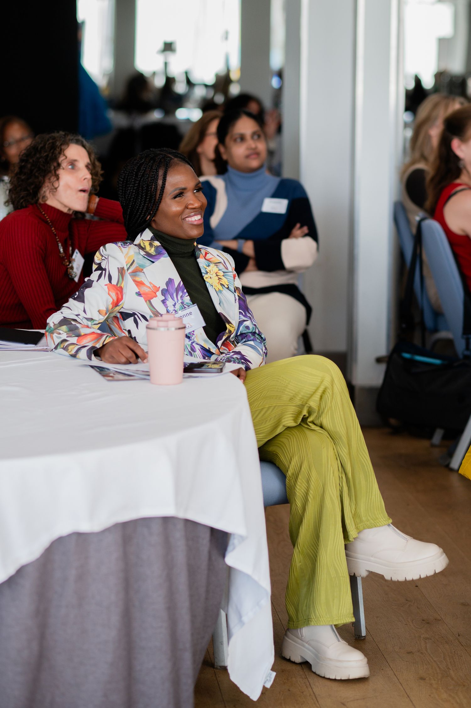 Guests seated at tables with white tablecloths share conversation and laughter during an indoor social gathering.