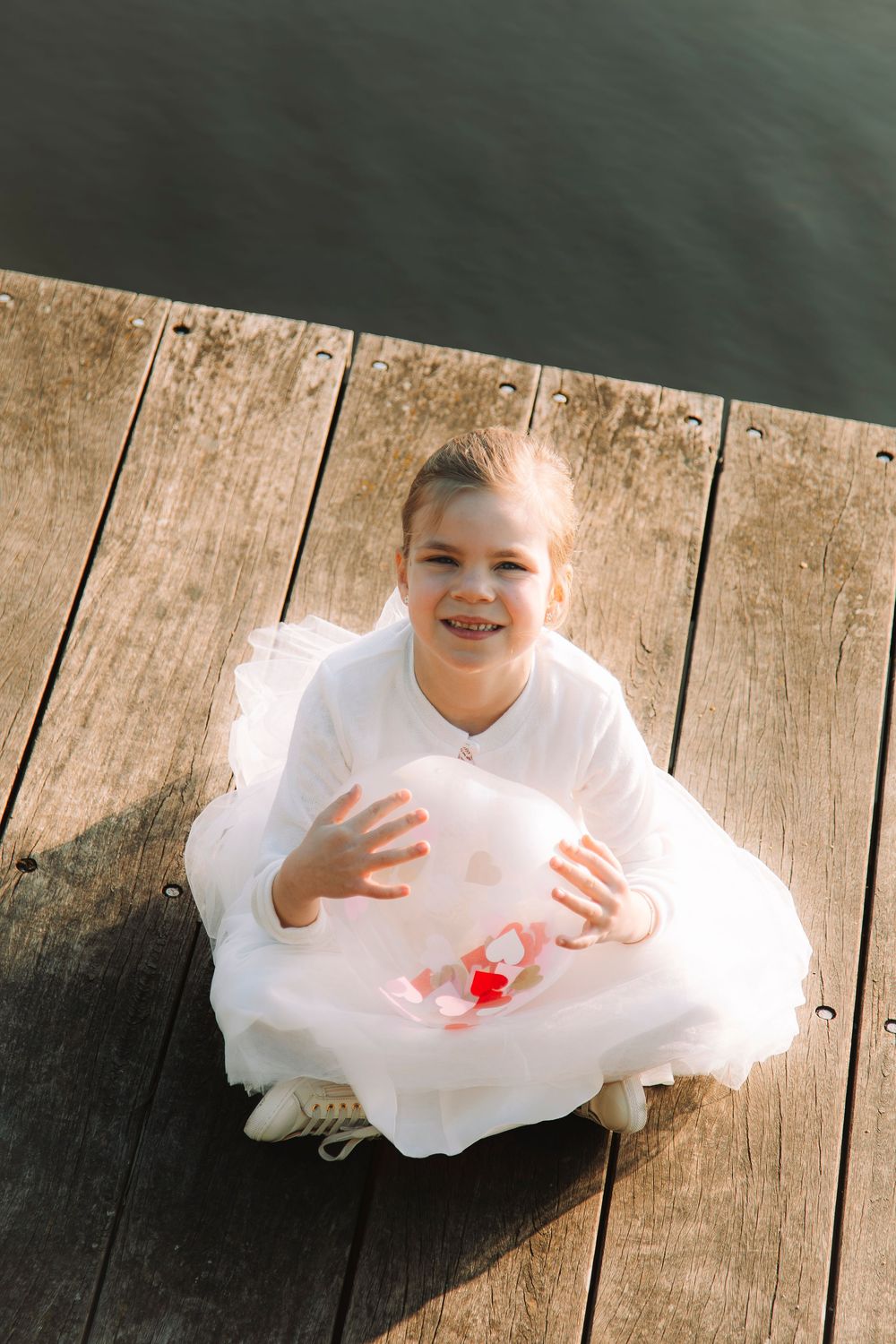 Meisje in een witte jurk en een ballon tijdens een communieshoot aan het water.