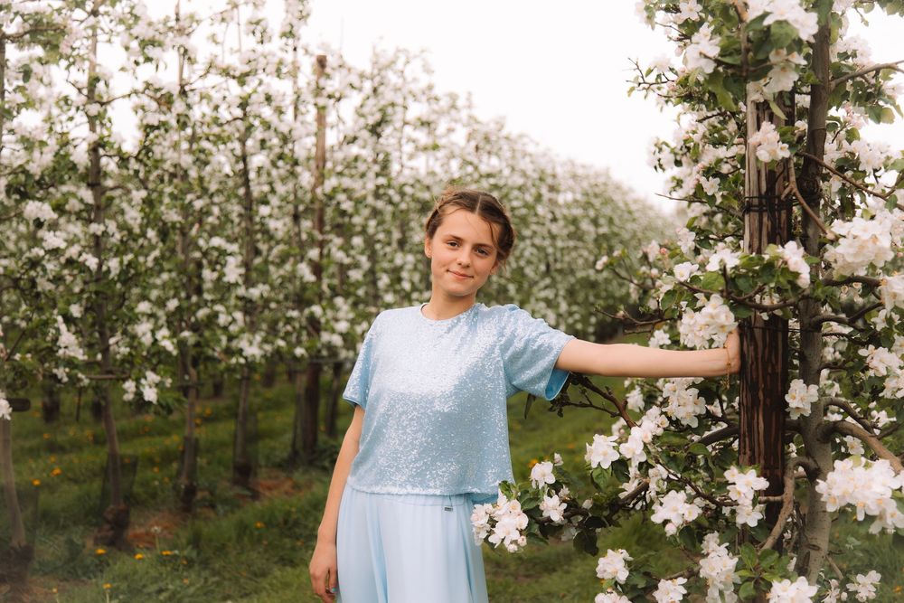 Meisje in blauwe jurk tijdens een communieshoot tussen bloesems.
