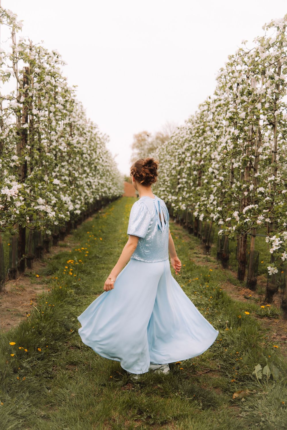 Meisje in blauwe jurk tijdens een communieshoot tussen bloesems.