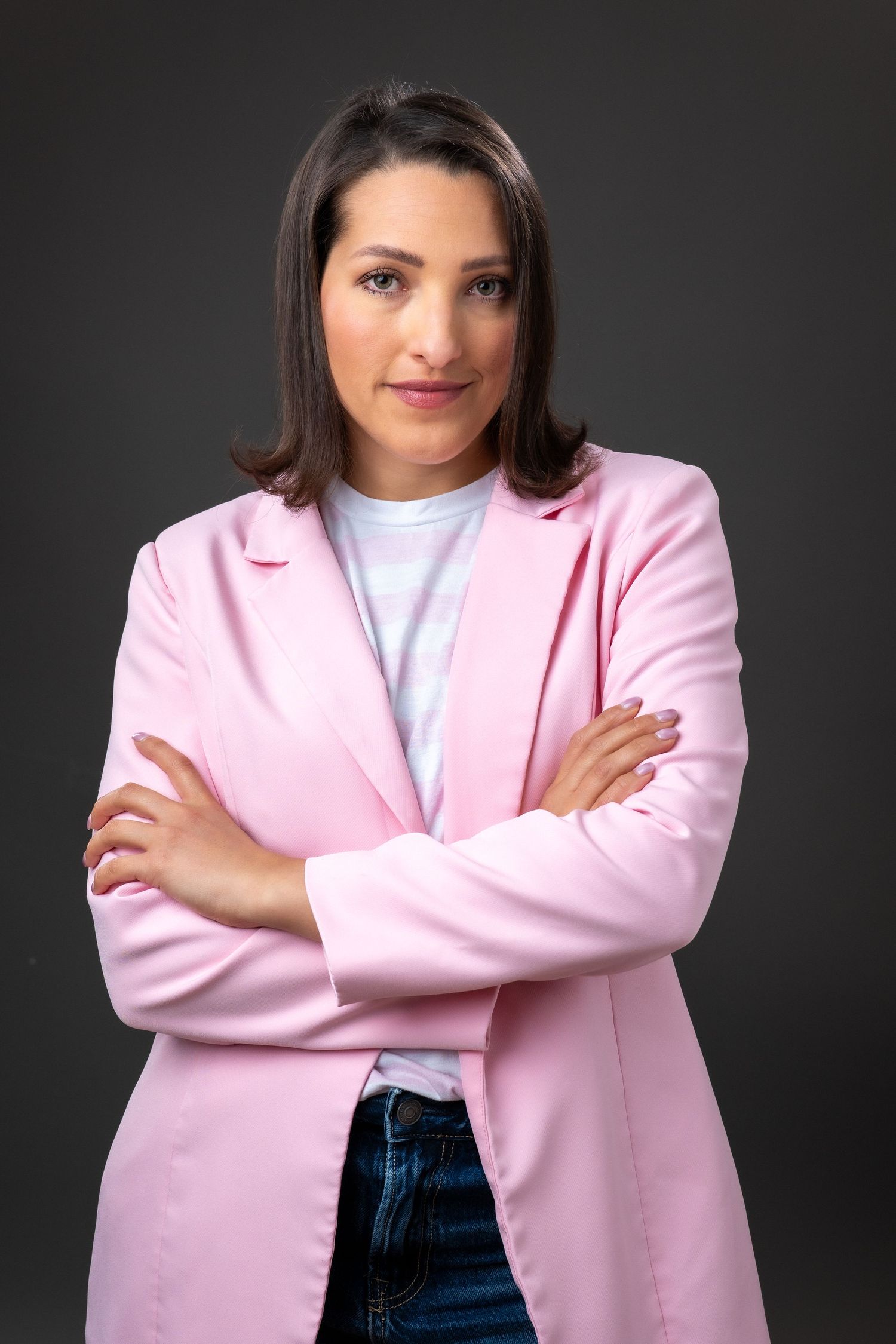 Professional studio portrait of someone wearing a pink blazer and white top against dark background.