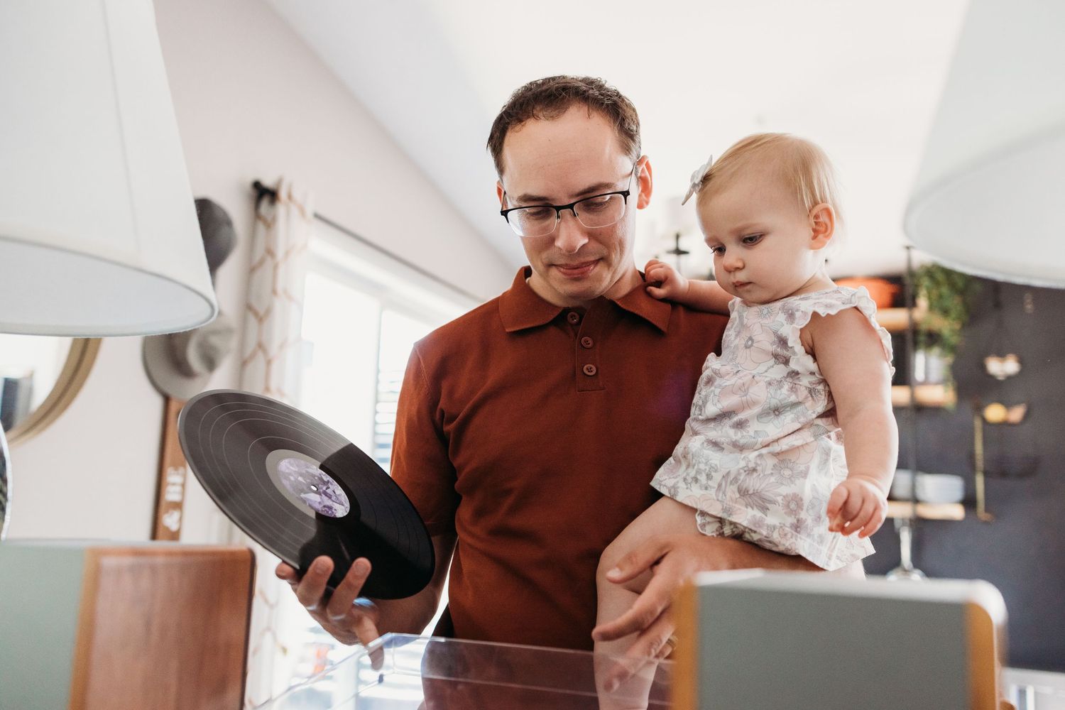 Adult in brown shirt feeding a baby in a modern kitchen while preparing food and doing various tasks.