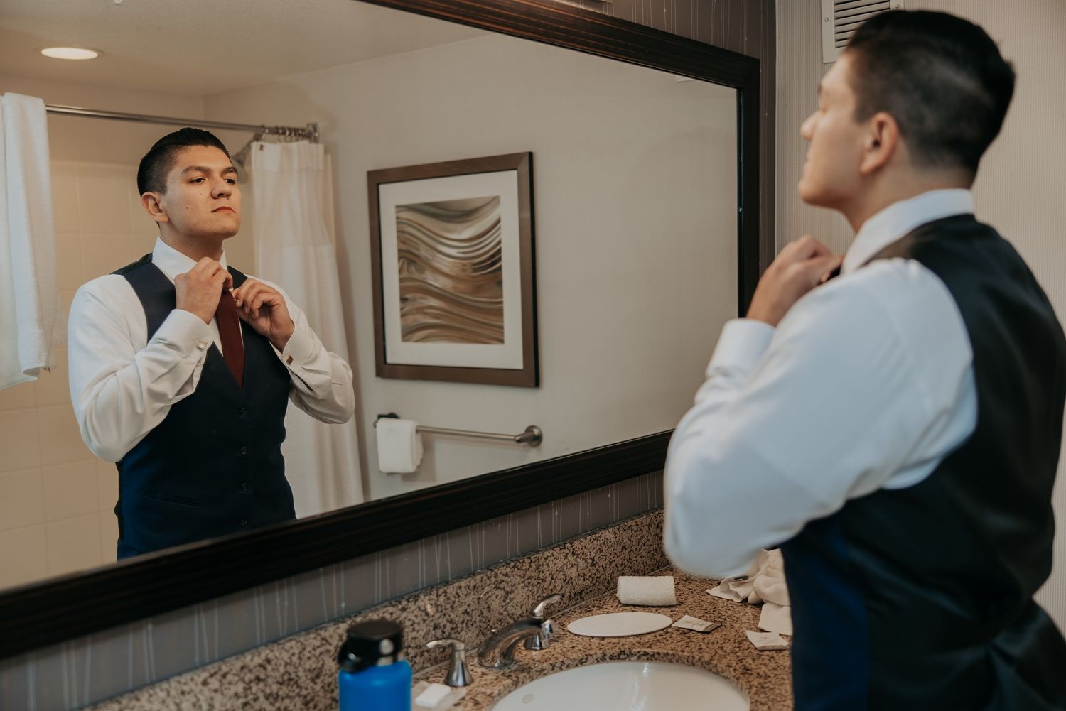 A groom in formal attire getting ready in front of a bathroom mirror.