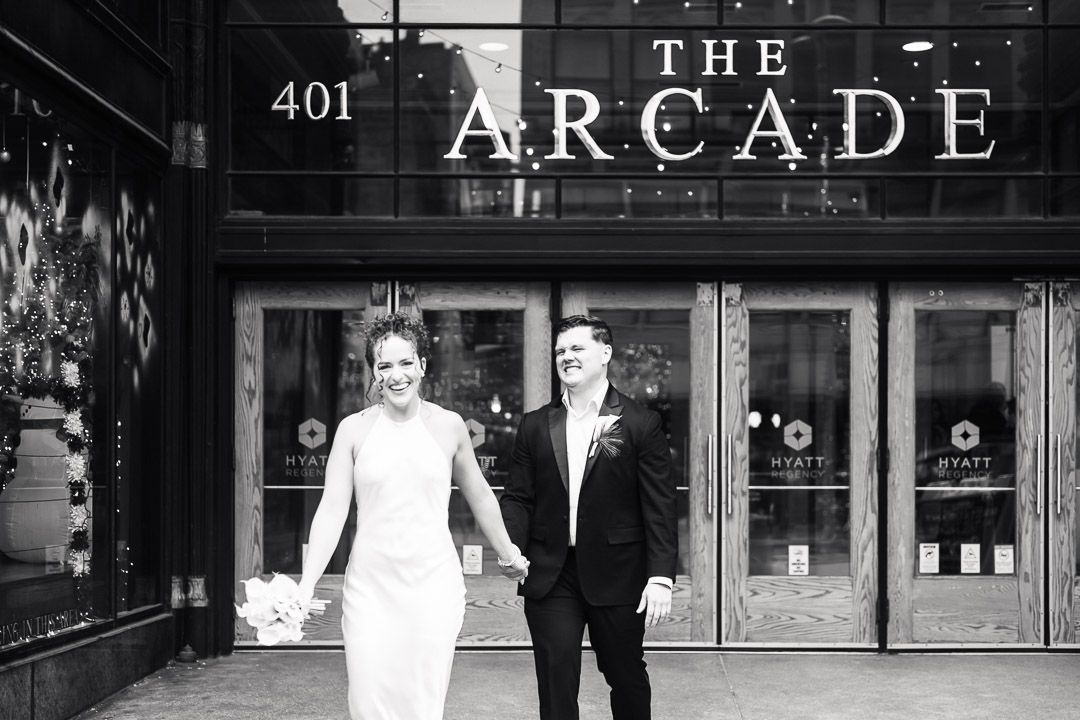 A black and white photograph of a bride and groom walking out of the Cleveland Arcade downtown.
