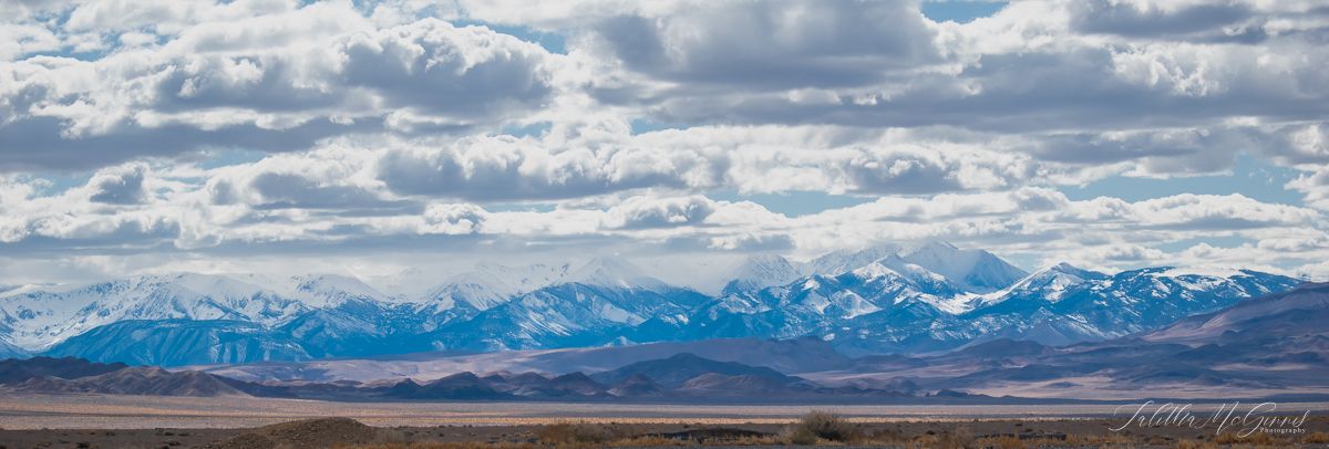 Panoramic view of snow-capped mountain ranges under dramatic cloudy skies stretching across the horizon.