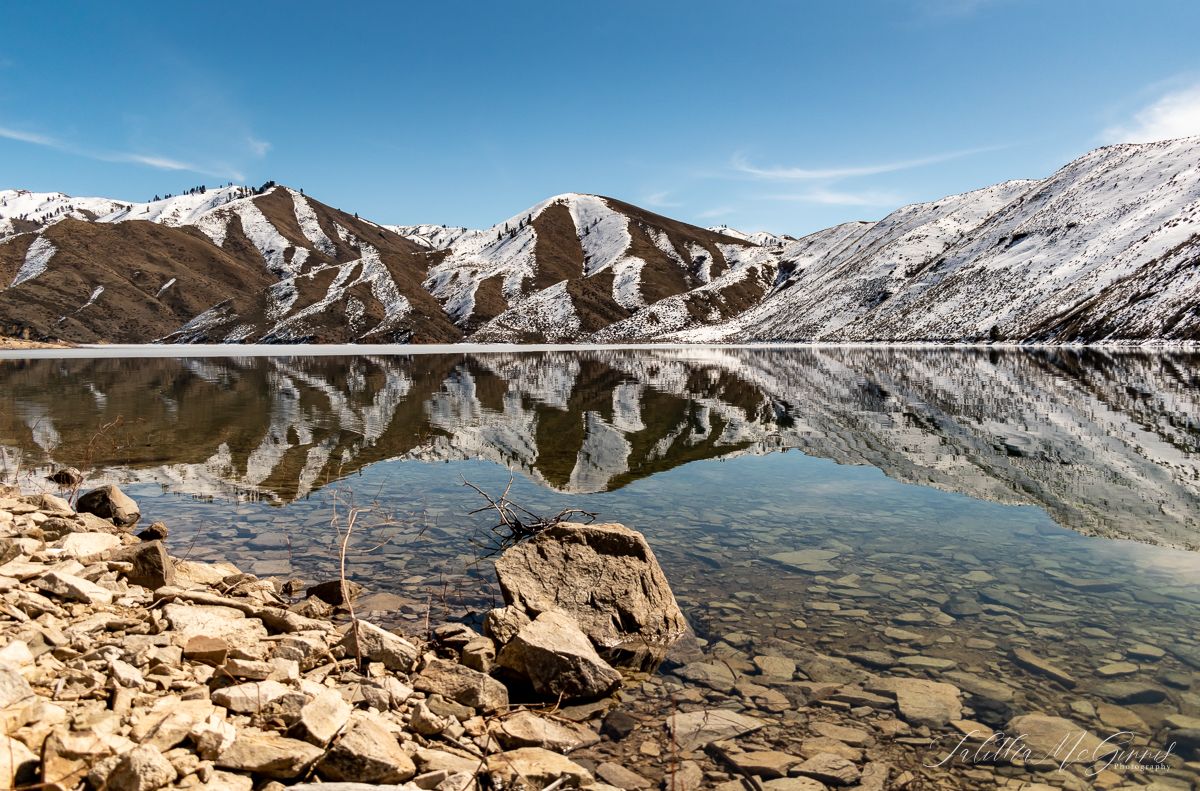 Panoramic view of snow-capped mountain peaks and rugged terrain under a bright blue sky in the wilderness.