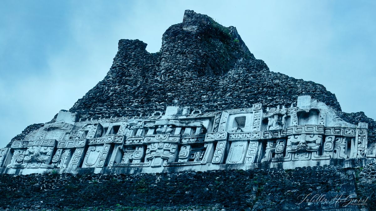 Ancient stone ruins of Xunantunich with terraced walls against a blue and cloudy sky.