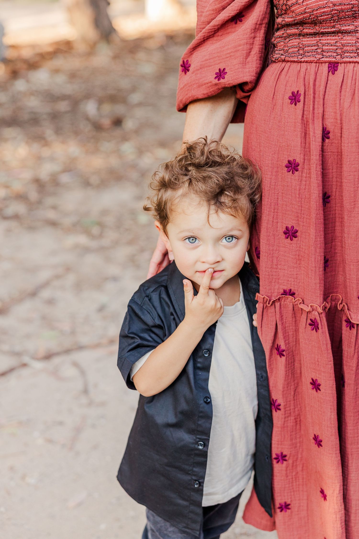 Small child in navy button-up shirt and gray t-shirt stands next to person wearing red floral dress.