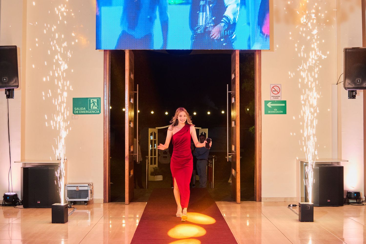 A person in a flowing red satin gown poses elegantly on wooden steps decorated with greenery and floral arrangements.