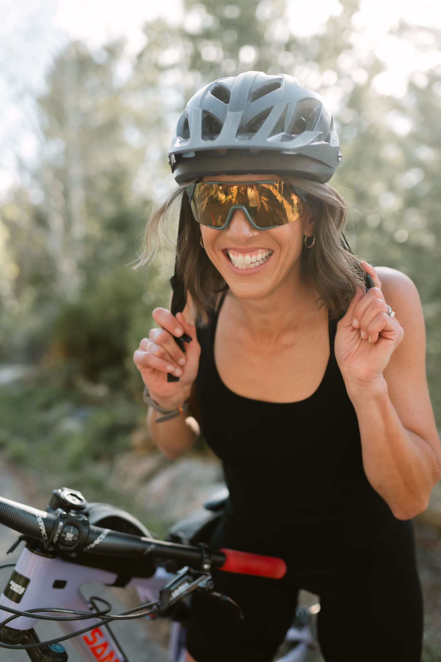 Colorado branding photographer smiling while putting on bike helmet outdoors, active lifestyle portrait