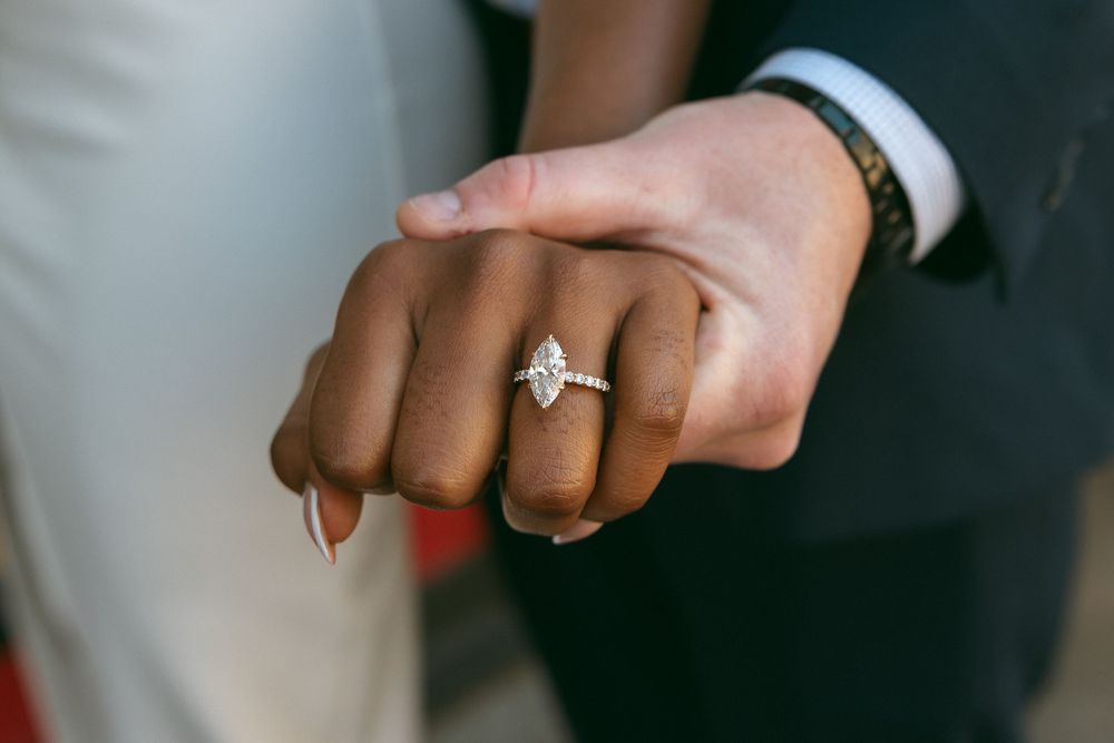 Close-up shot of hands with engagement ring and wedding band against a dark background.