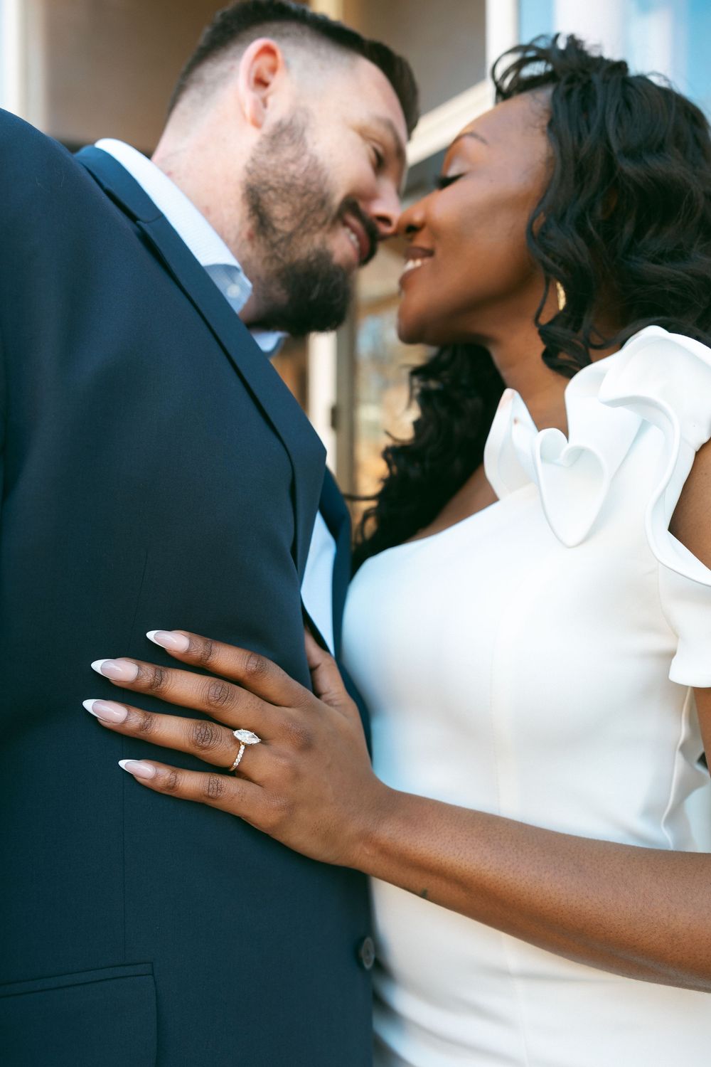 A romantic couple shares an intimate moment in formal attire against a neutral background.