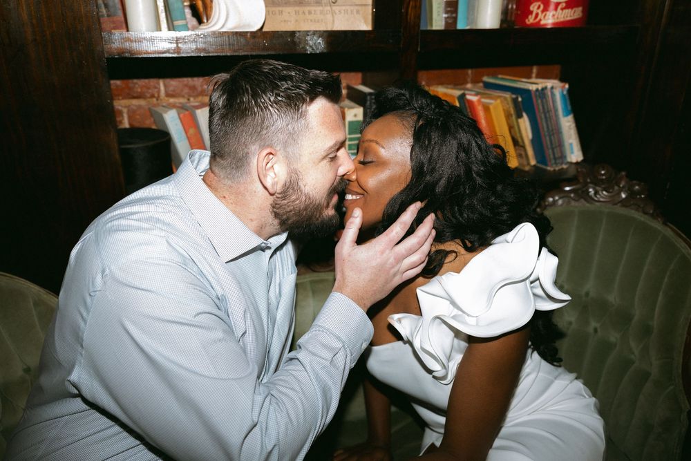 Two people in white shirts embrace and share an intimate moment at a dimly lit venue.