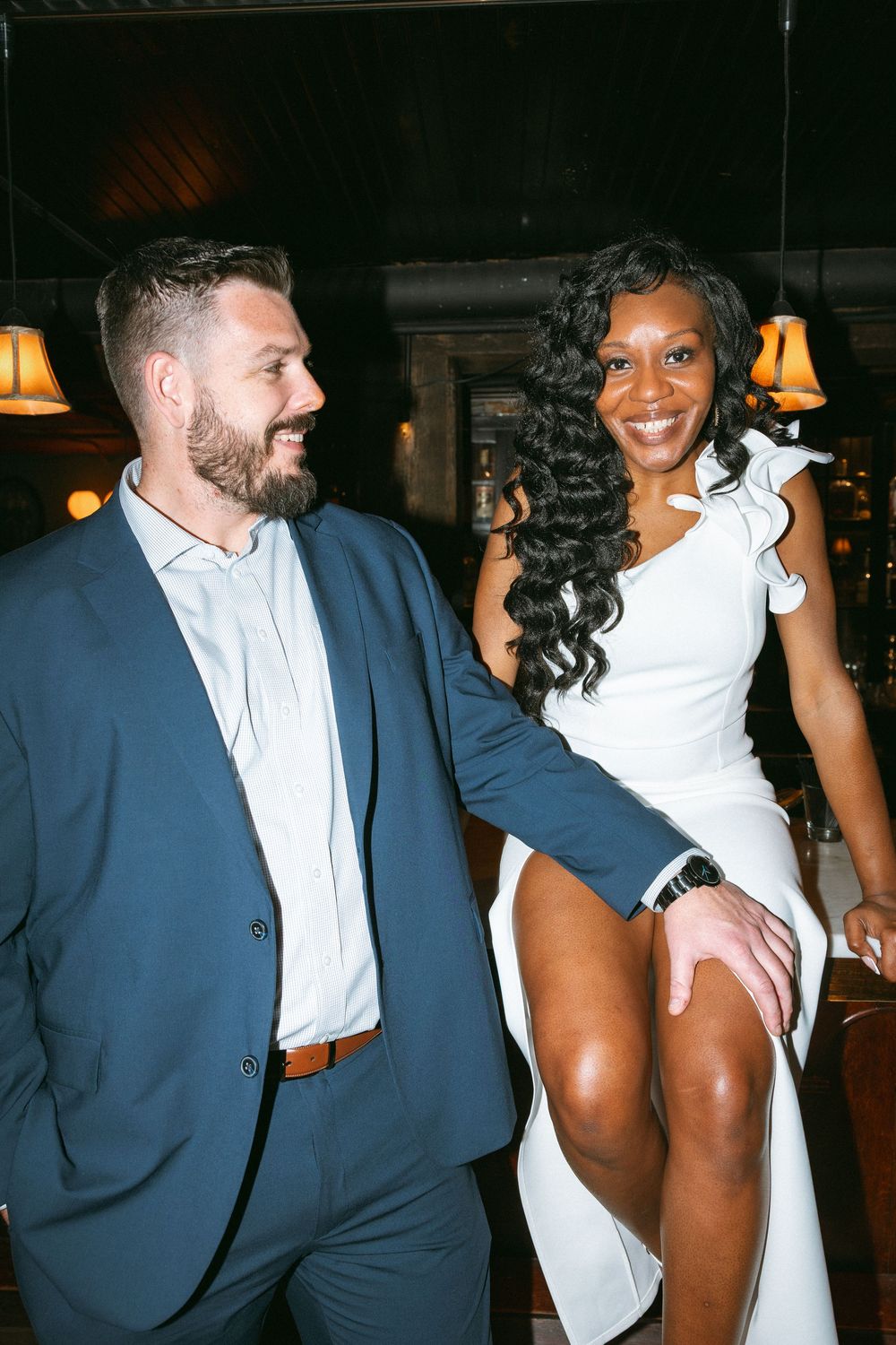 A couple shares a candid moment together at an evening event, dressed in formal attire.