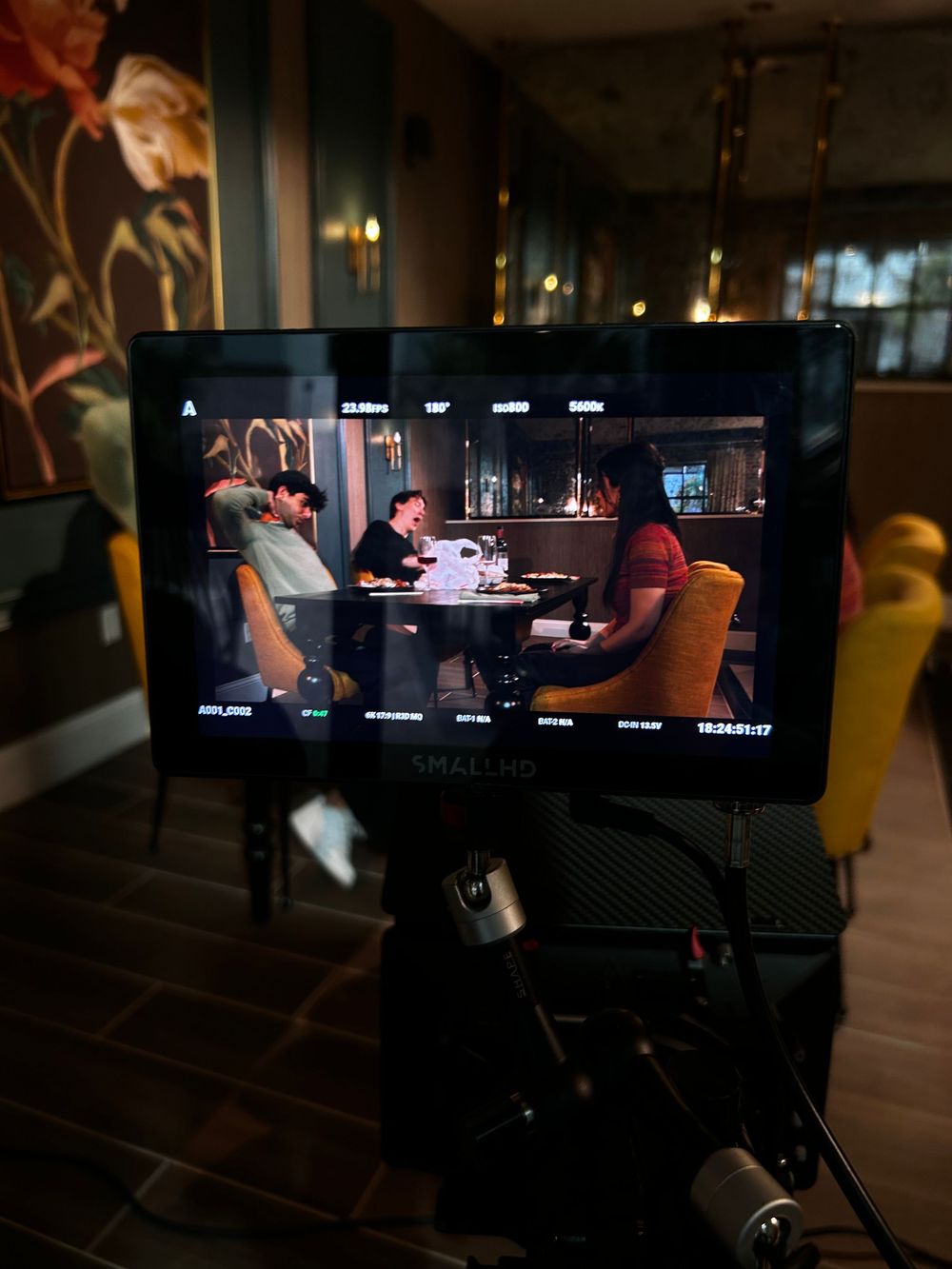 Behind-the-scenes view of a dimly lit video production set with monitors and camera equipment visible in the background.