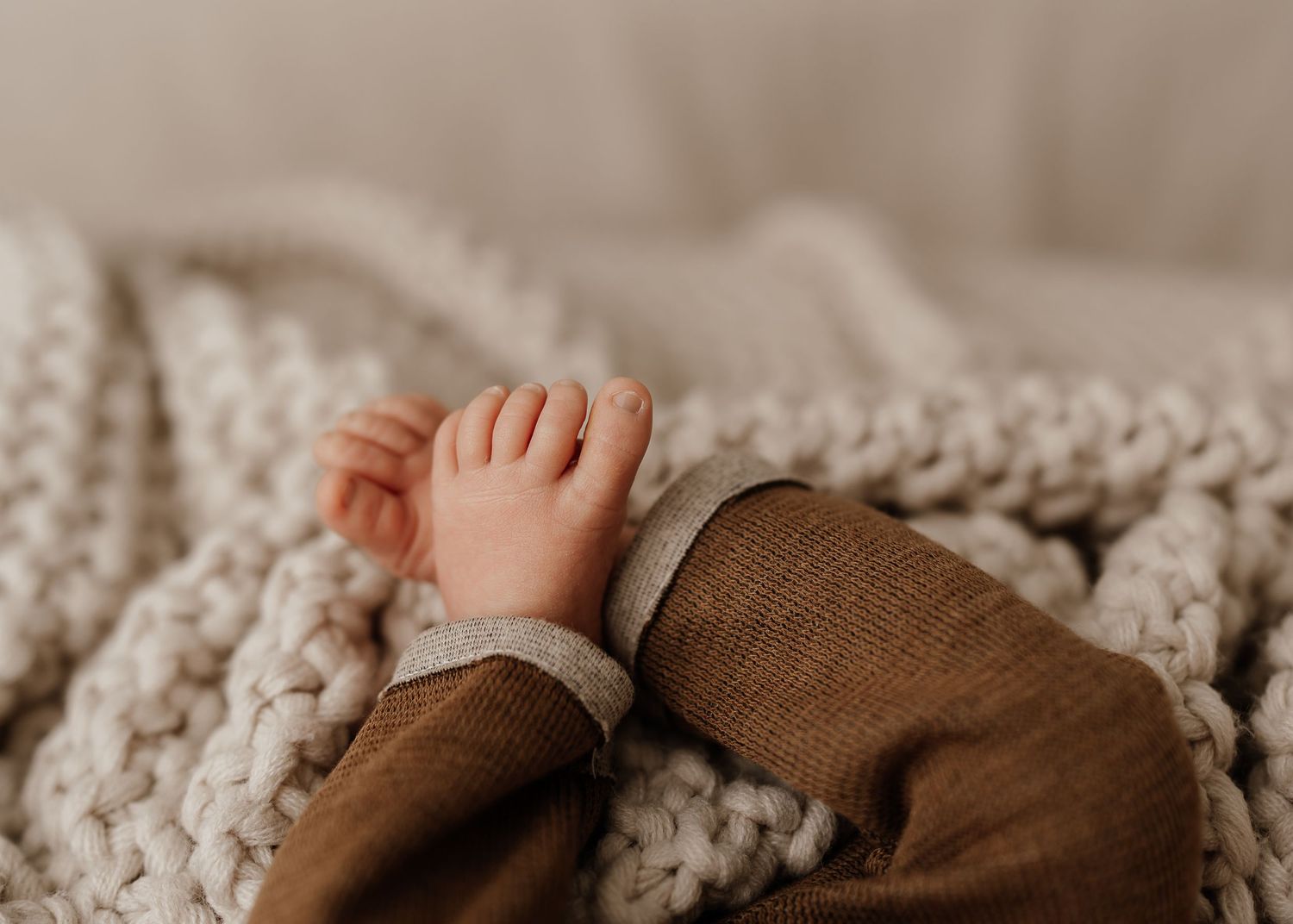 A sleeping infant dressed in white lies on a soft white surface in a series of gentle stretching poses.