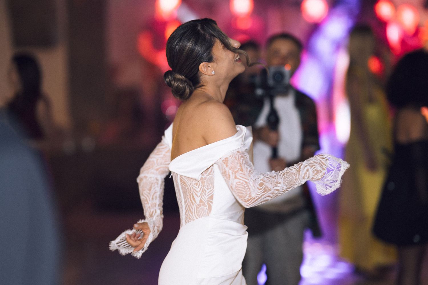 Bride in off-shoulder lace wedding gown laughing joyfully while dancing at elegant wedding reception.