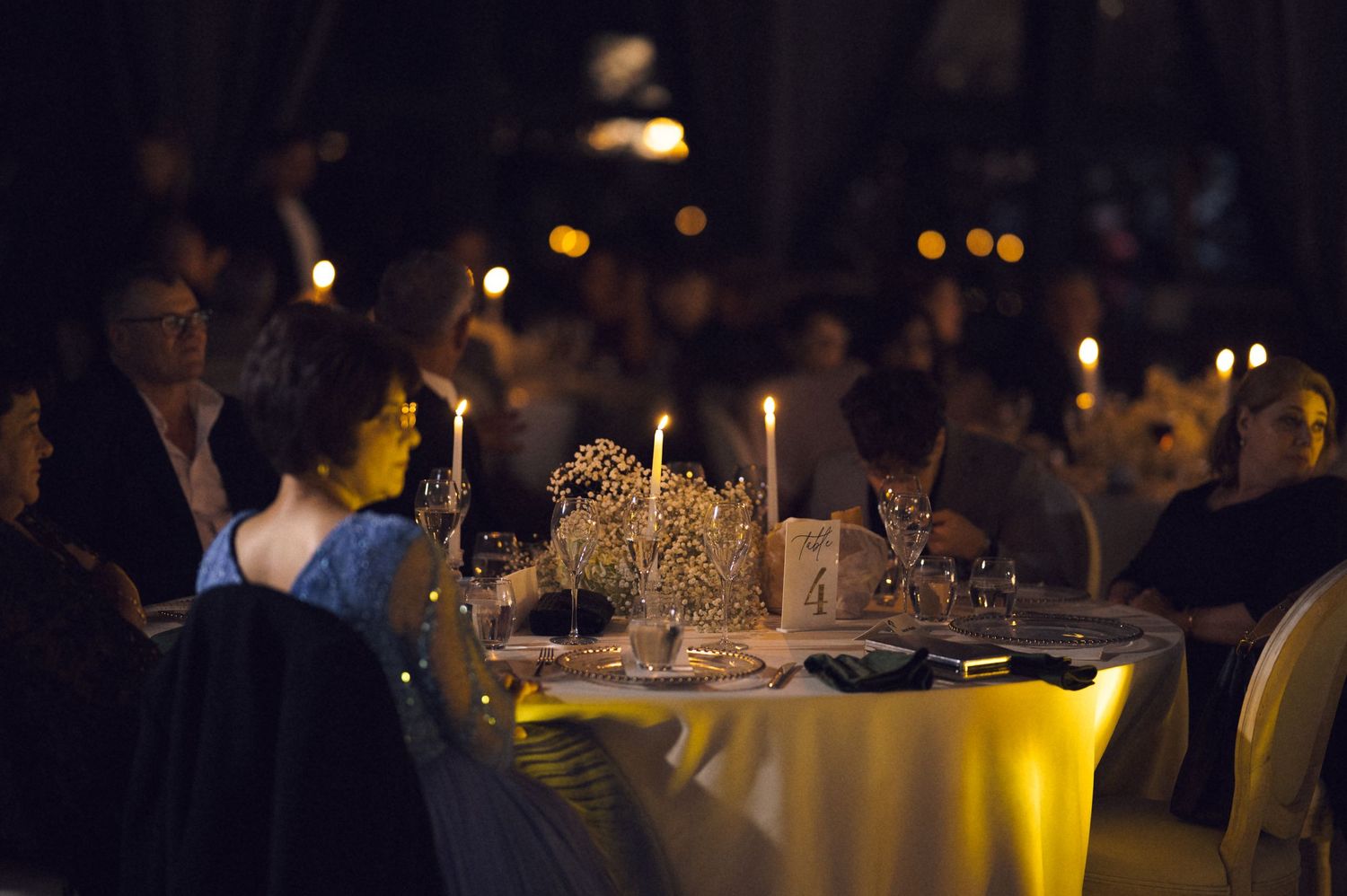Elegant candlelit dinner party with guests seated at round tables in a dimly lit formal event venue.