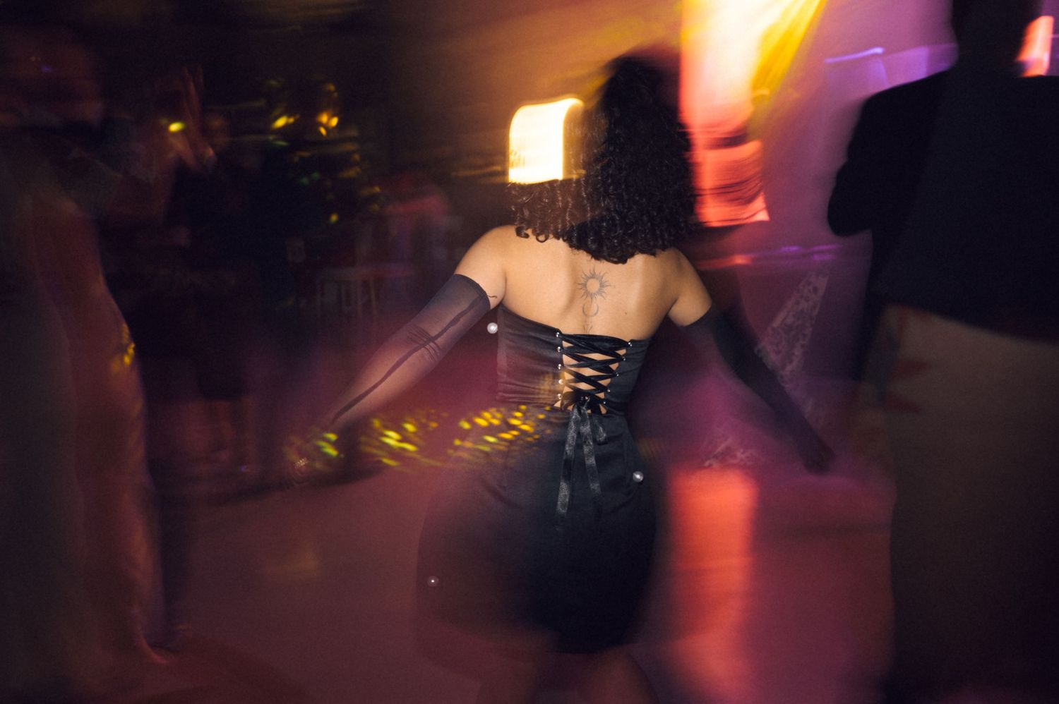 Woman in black corset dress dancing at evening wedding reception with motion blur effect.