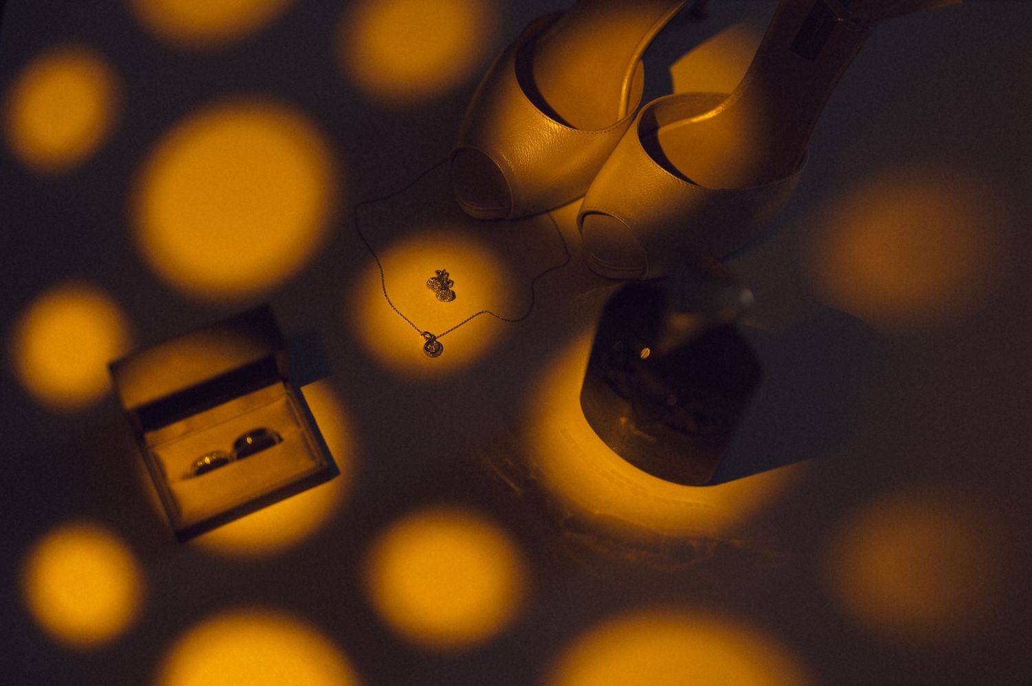 Golden bokeh light circles illuminate wedding rings, a necklace, and bridal heels in a romantic flat lay.