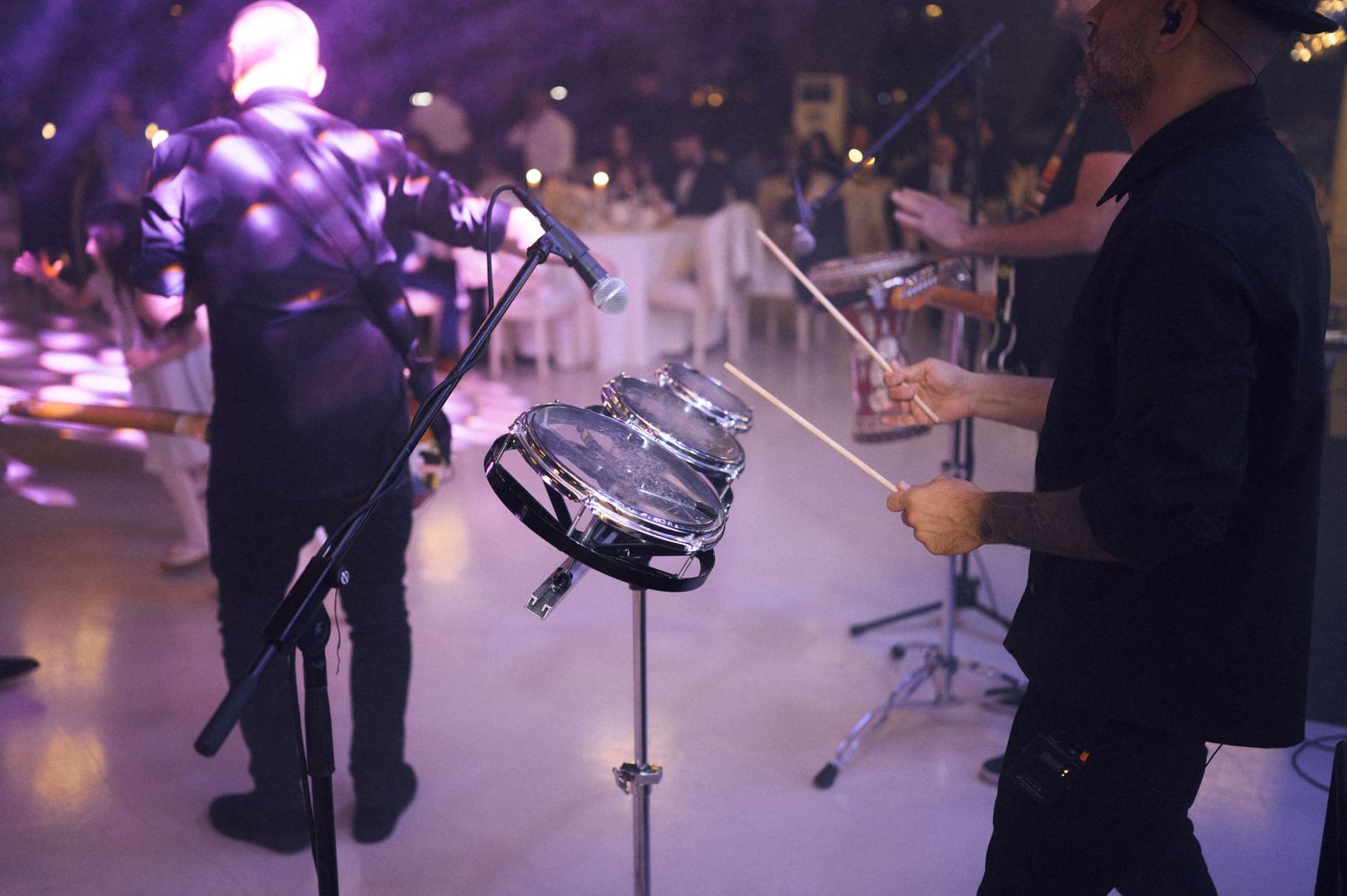Musicians performing live at an elegant event, playing steel pan drums on stage with purple ambient lighting.