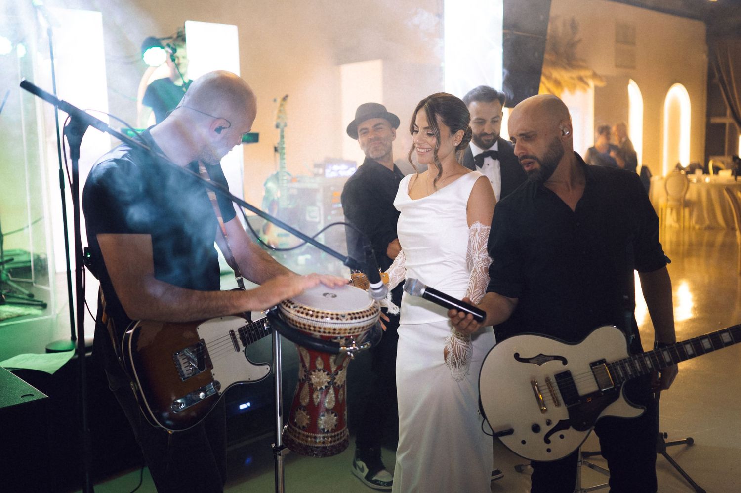 Bride and groom celebrate with live band at wedding reception, guitarist and drummer performing on stage.