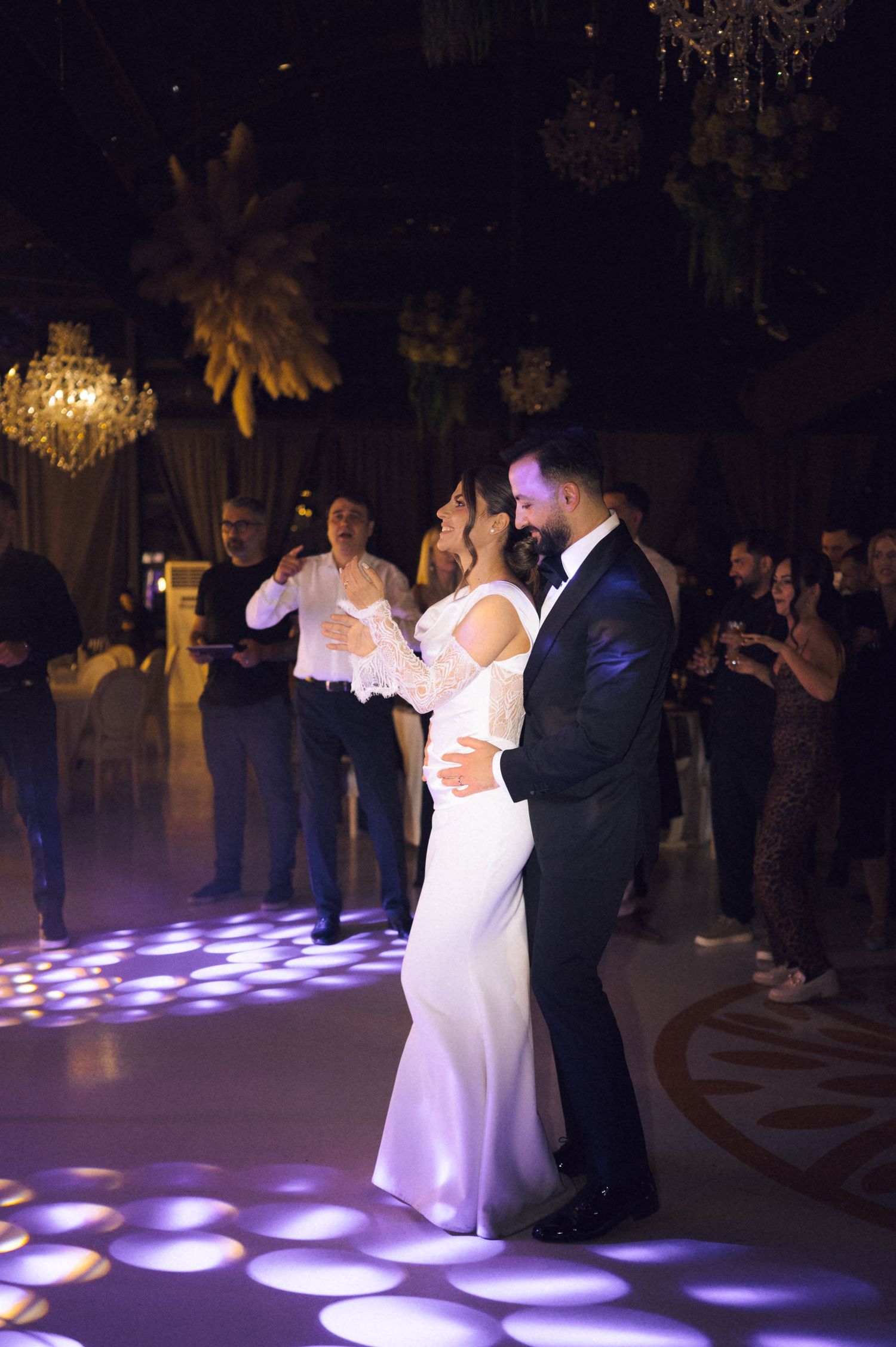 Bride and groom share their first dance on a spotlit dance floor surrounded by guests at an elegant wedding reception.