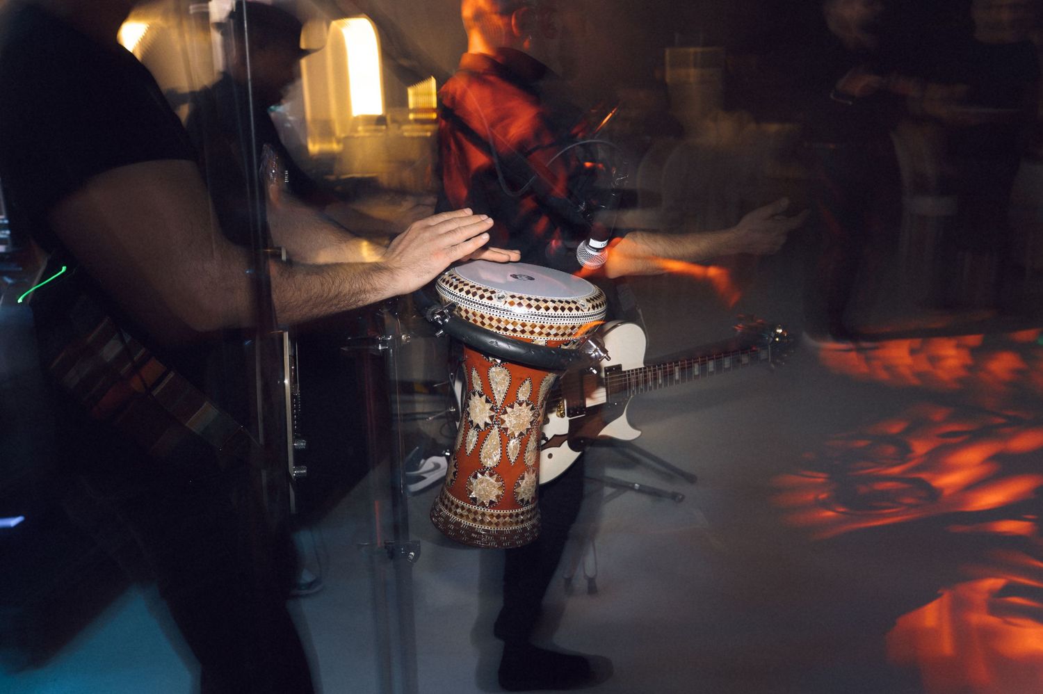 Musicians playing a decorative djembe drum during a live performance in a dimly lit venue.