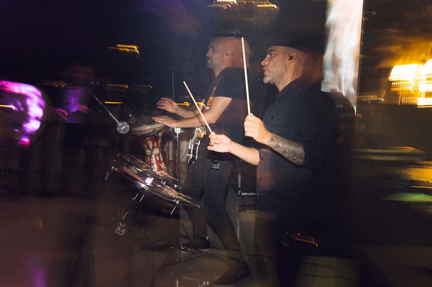 Two drummers performing live on stage in a dark venue, captured with motion blur during an energetic concert.