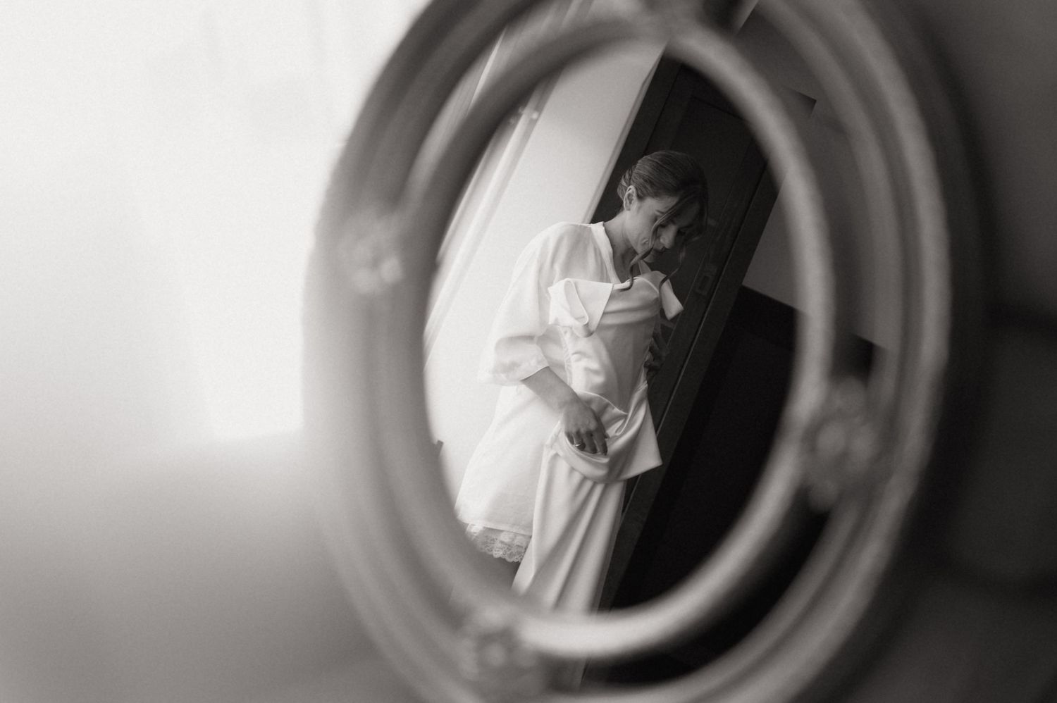 Black and white mirror reflection of a bride in a white gown sharing an intimate moment before her wedding ceremony.