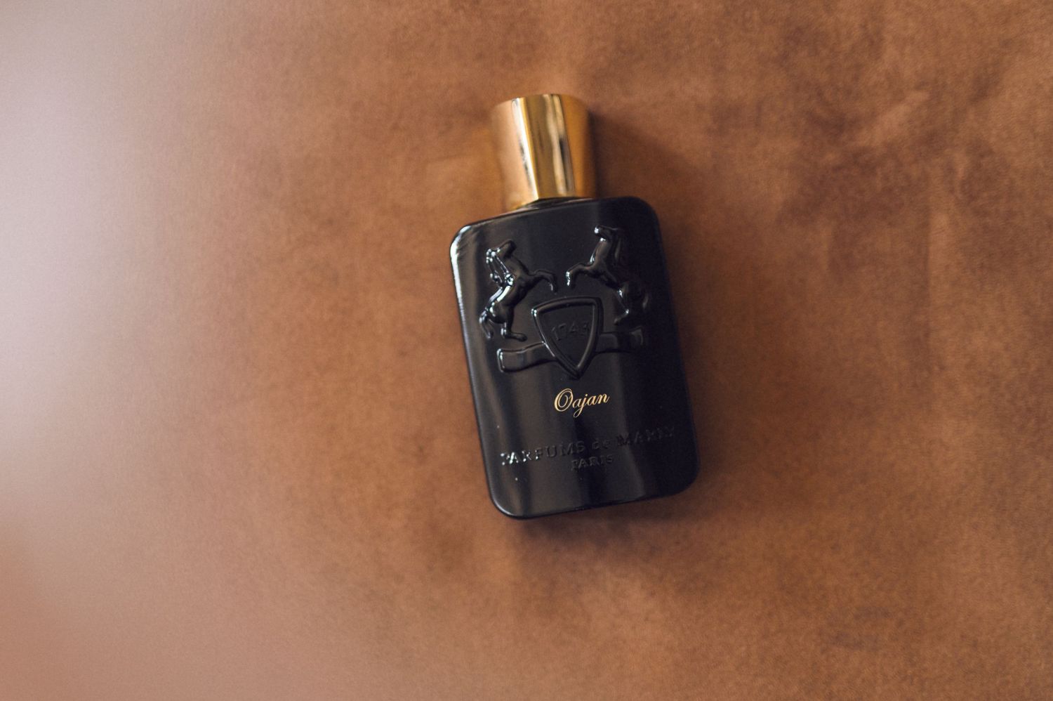 Parfums de Marly Oajan black and gold luxury eau de parfum bottle on brown leather surface.