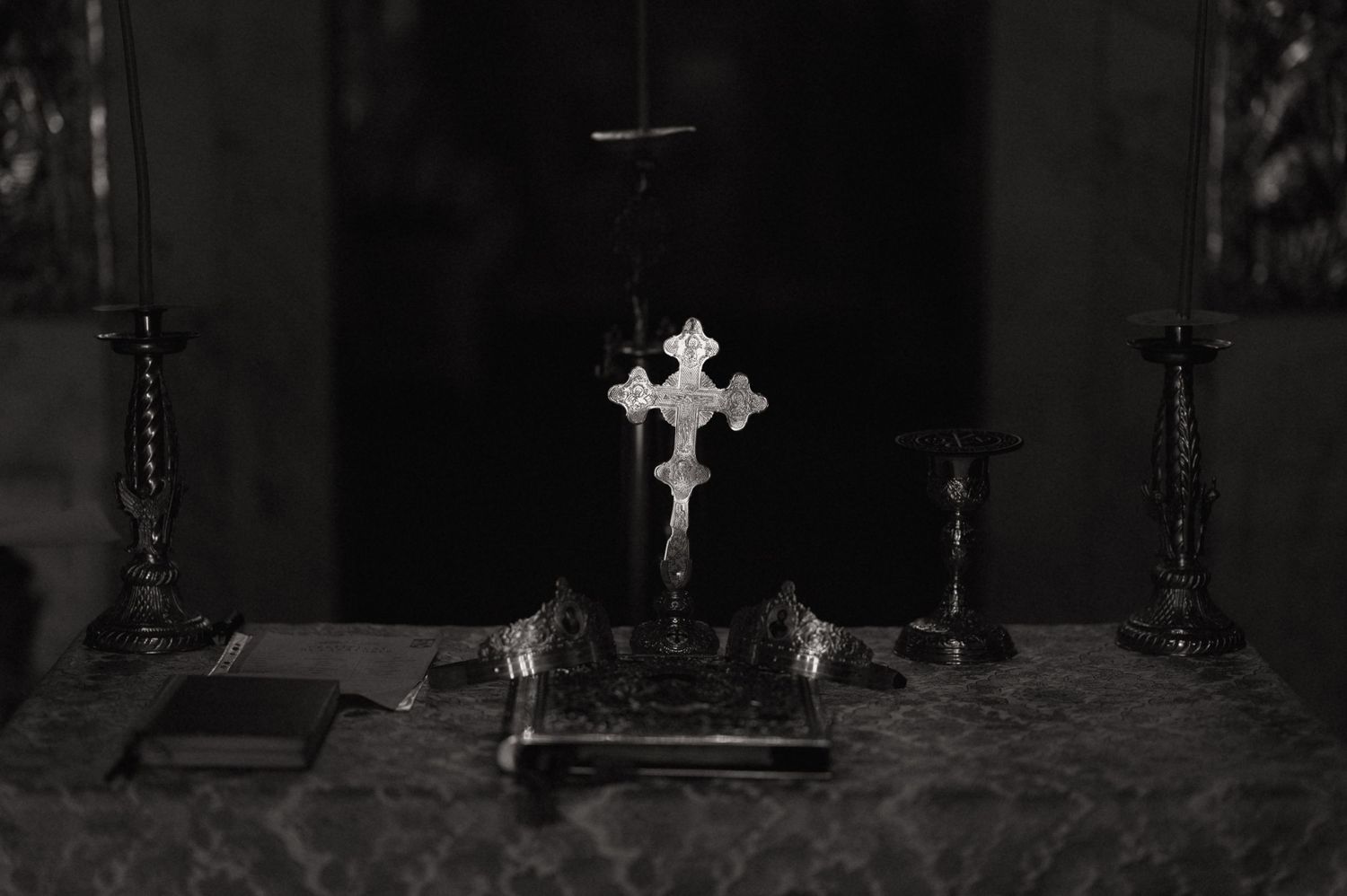 Black and white photo of a decorative cross on a church altar with candlesticks and holy books.