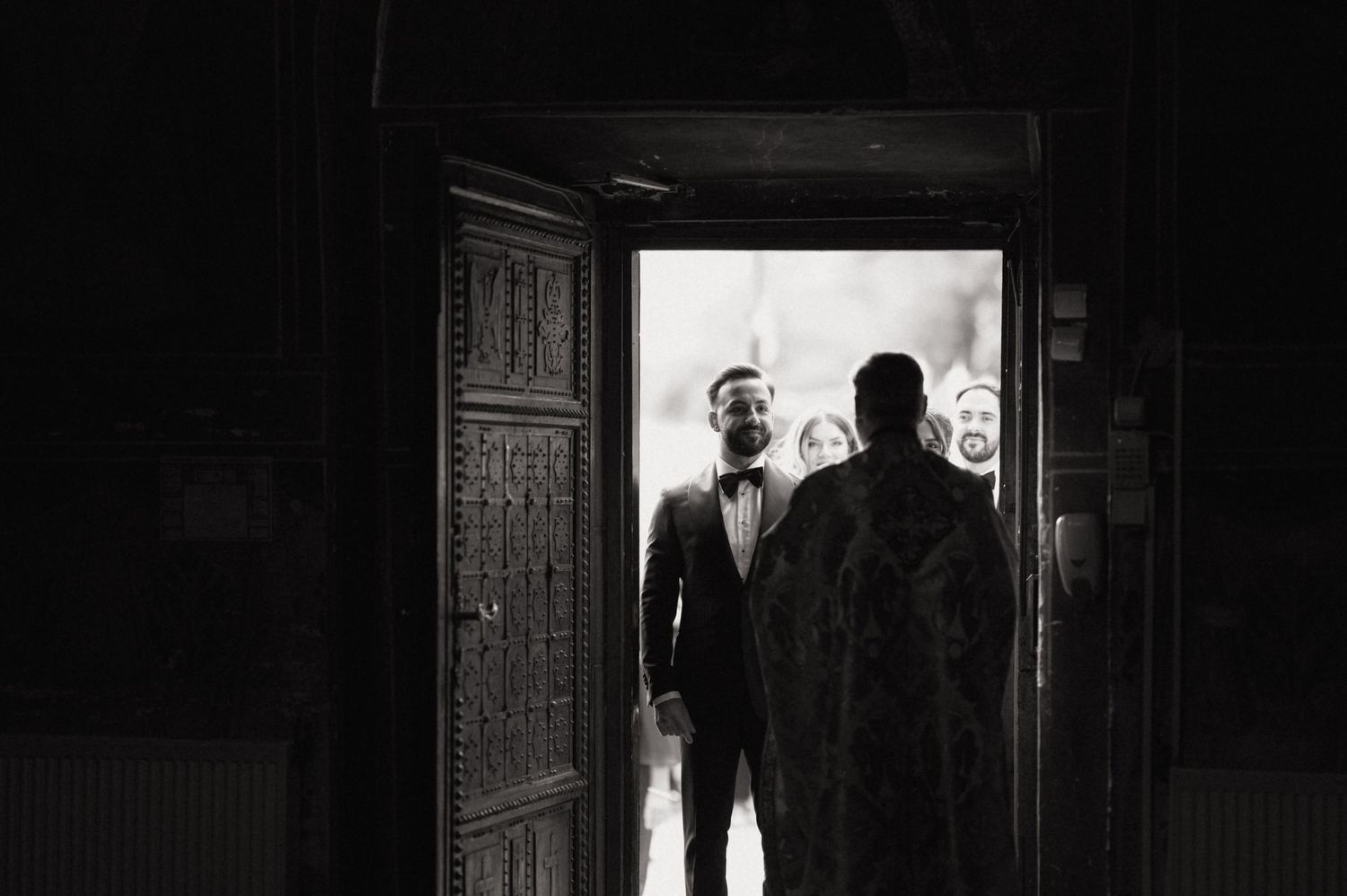 Black and white photo of two men in suits standing in an ornate doorway, one smiling at the camera.