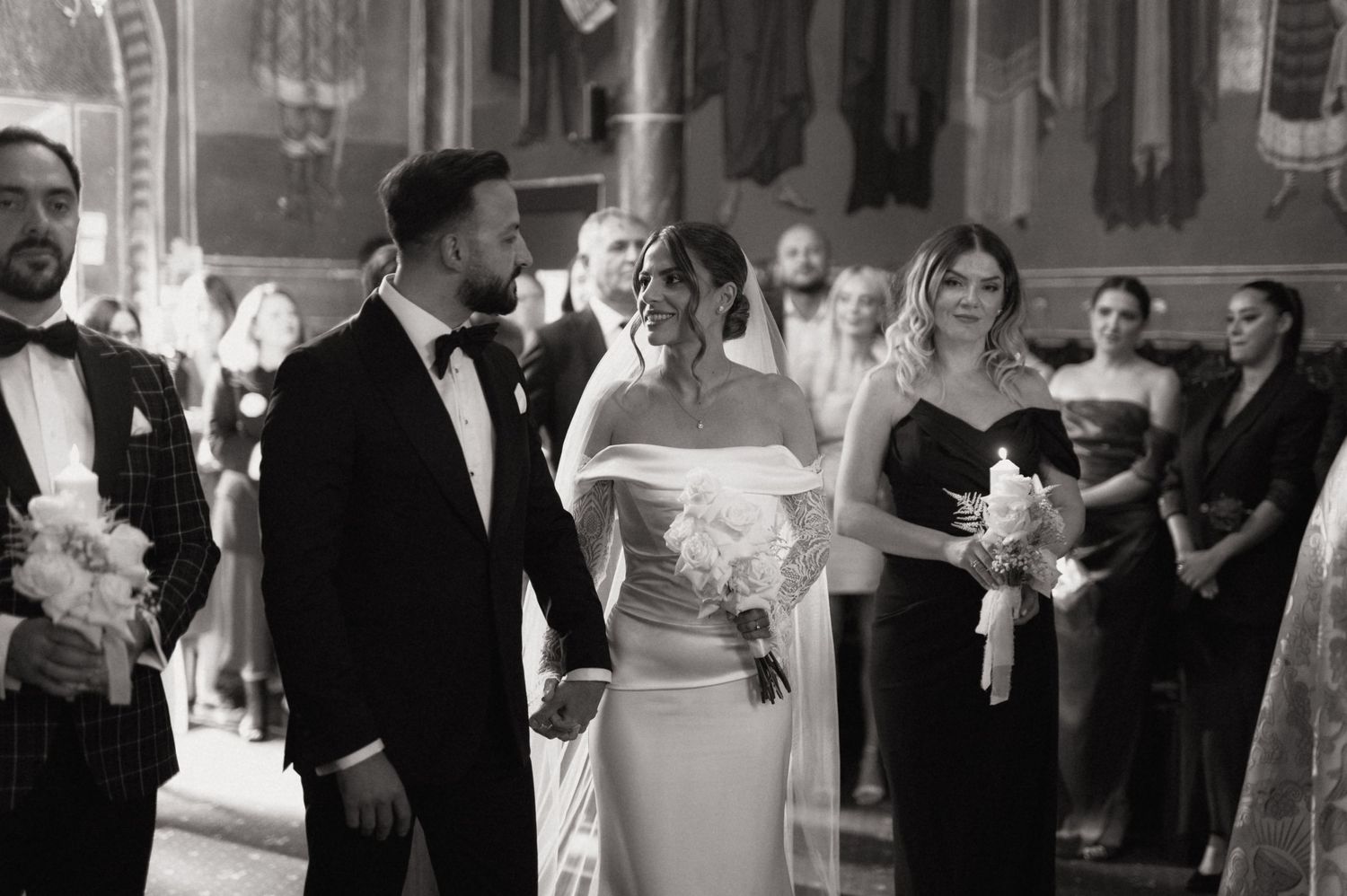 Black and white wedding ceremony photo of bride and groom walking down the aisle in an elegant church.