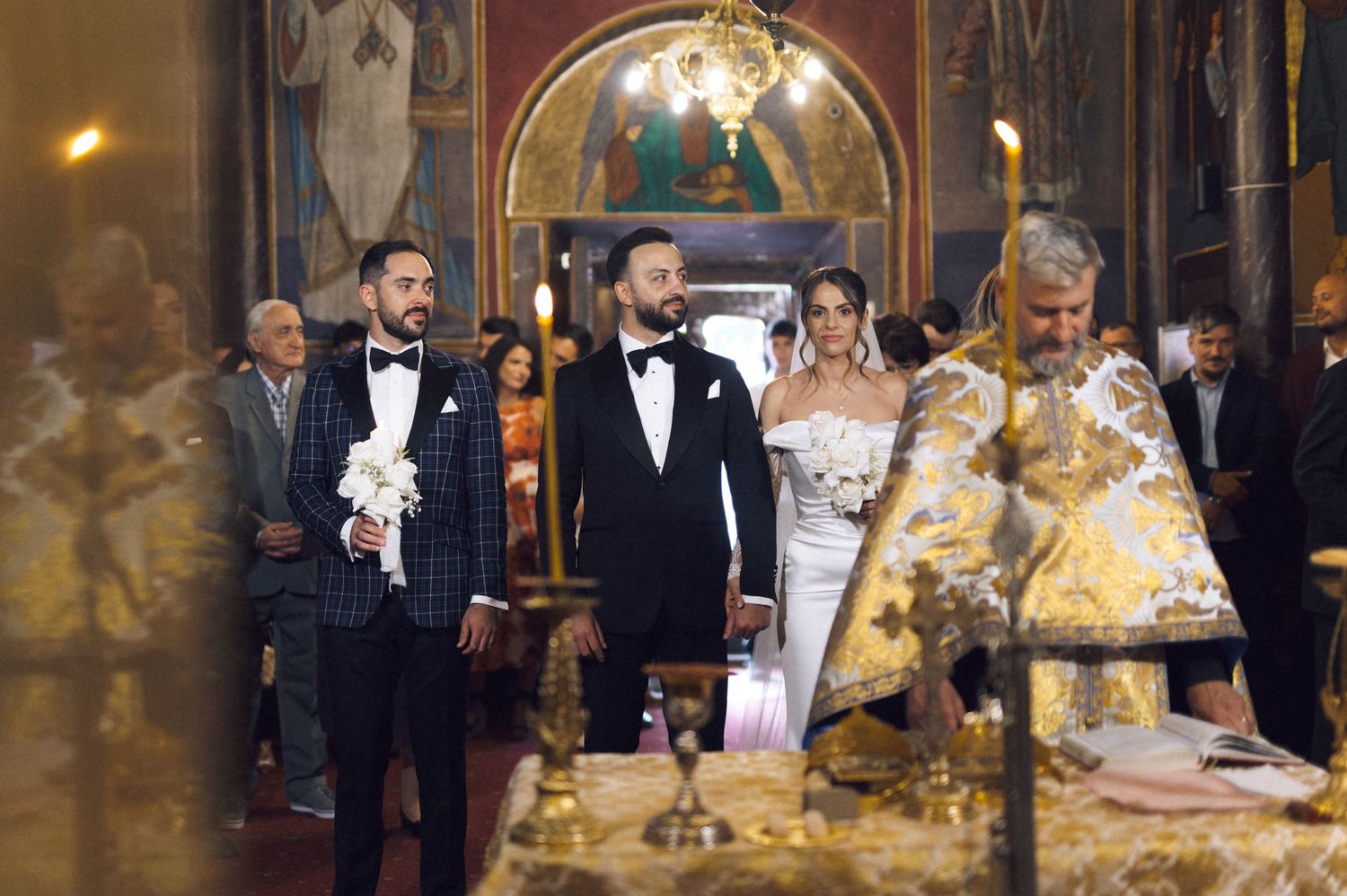 Orthodox wedding ceremony in ornate church with groom, best man, and bride in elegant attire.
