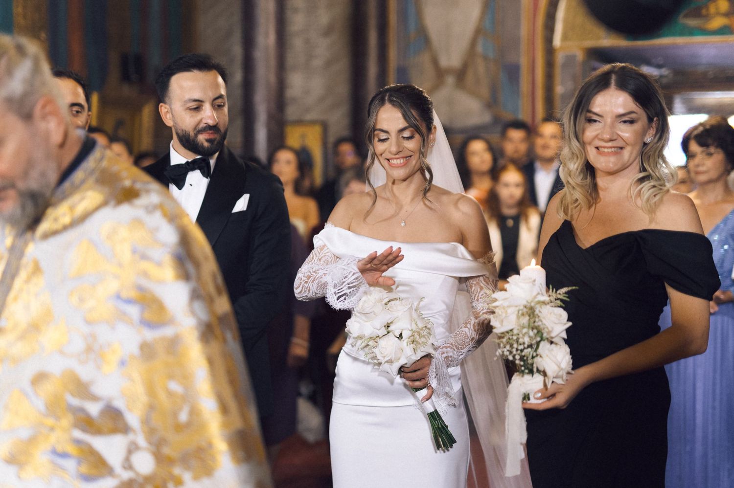 Bride walks down the aisle in white gown holding bouquet at Orthodox church wedding ceremony.