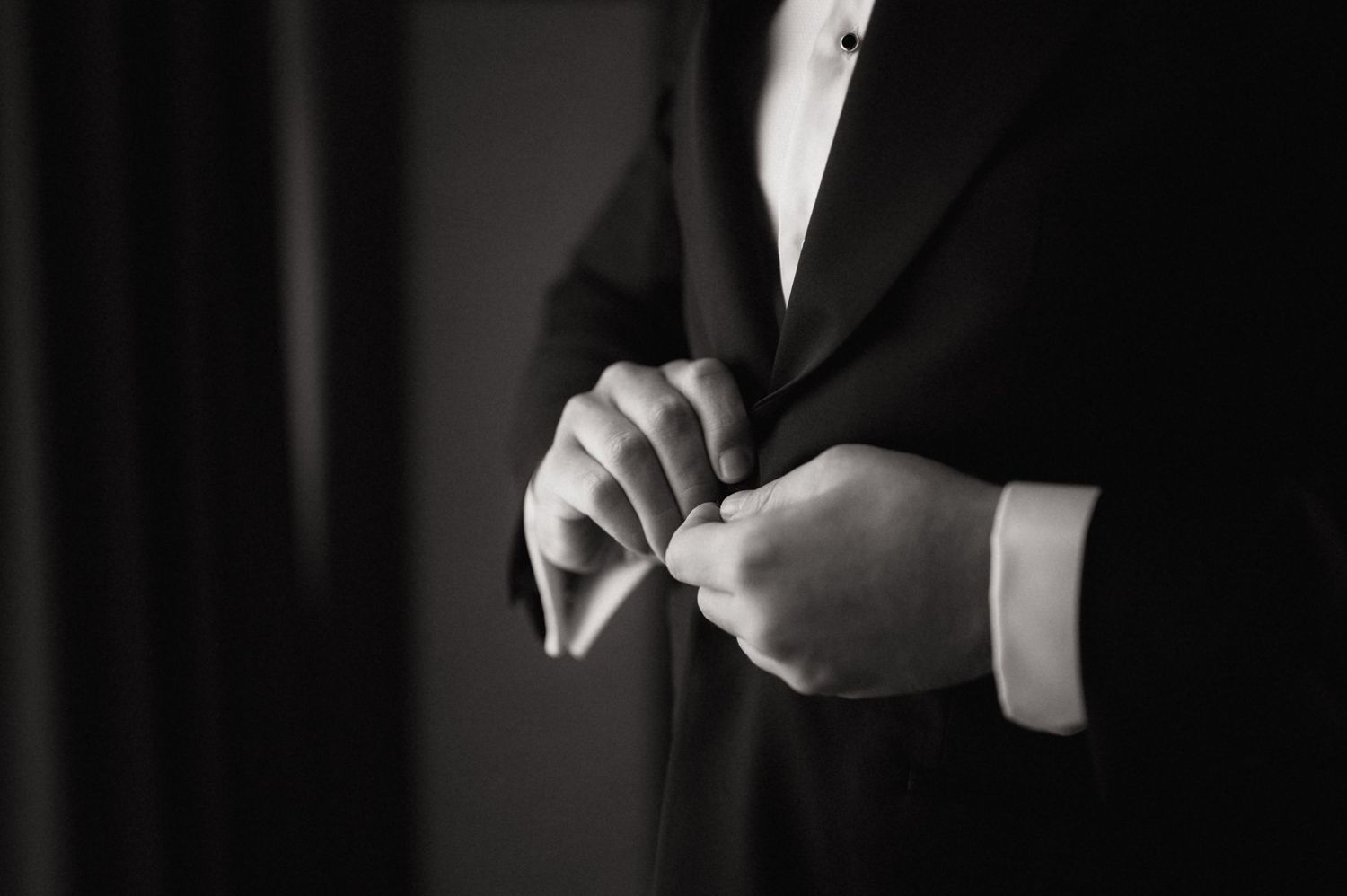 Black and white photo of a man in a suit buttoning his jacket, elegant formal attire detail shot.
