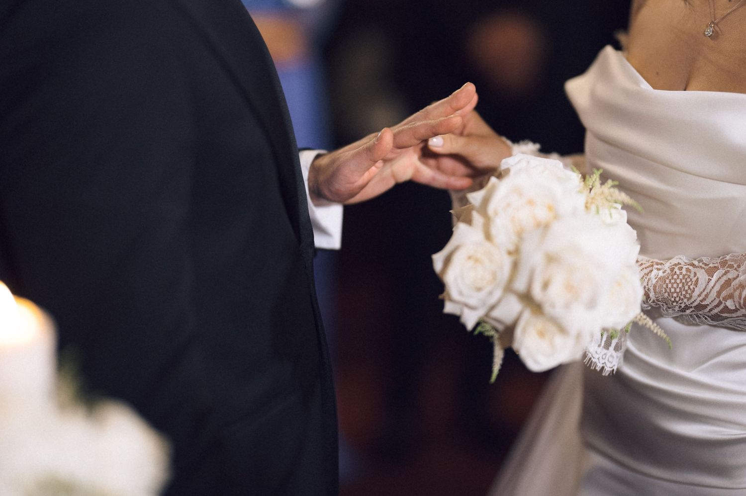 Bride and groom hold hands during wedding ceremony, bride holding white rose bouquet.