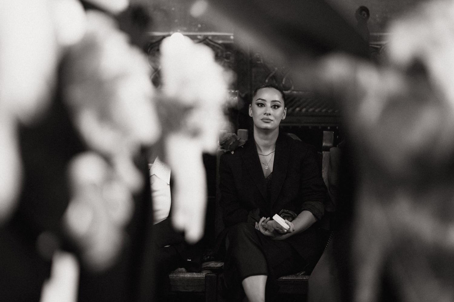 Black and white photo of an elegant woman in a black blazer seated confidently in a softly blurred background.