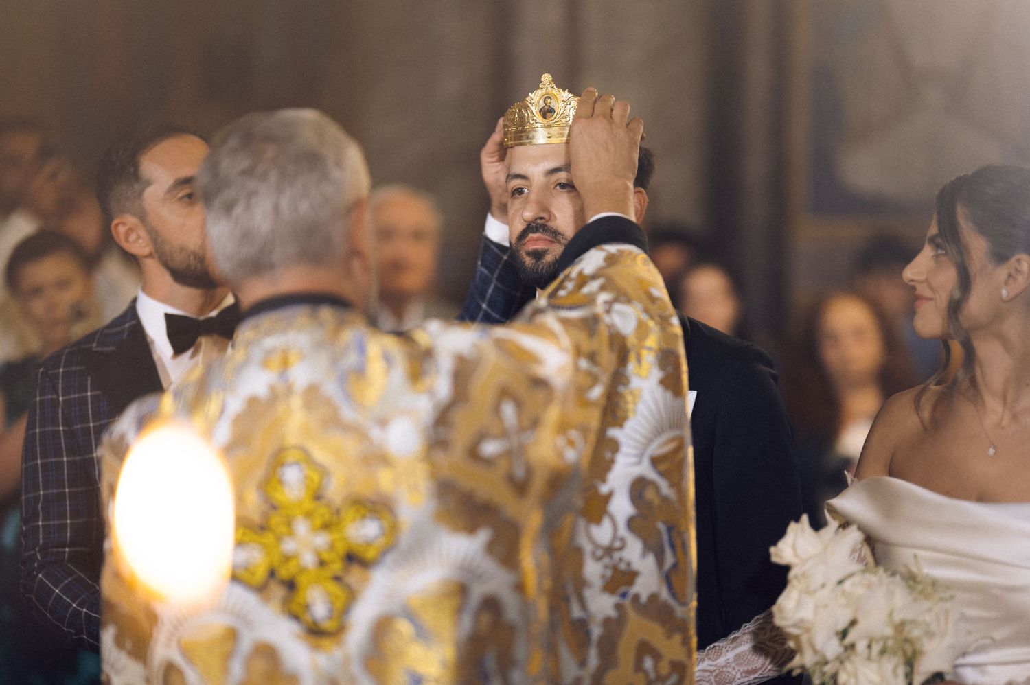 Orthodox priest placing crown on groom during traditional church wedding ceremony with bride beside him.
