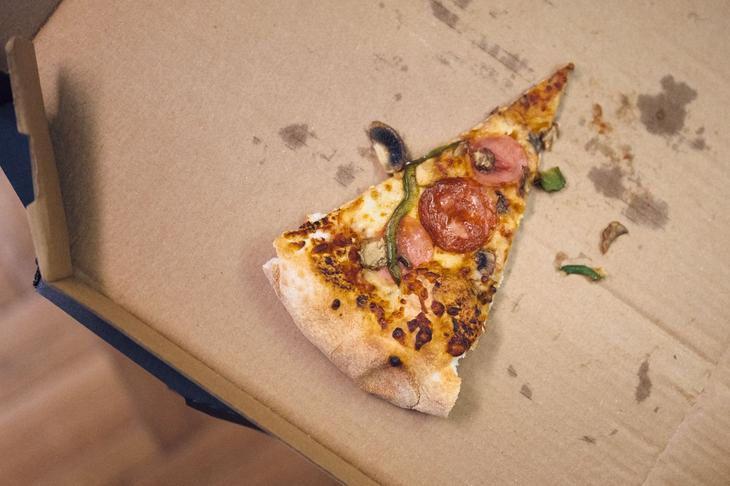 A single slice of pepperoni and tomato pizza with melted cheese sitting in an open cardboard delivery box.
