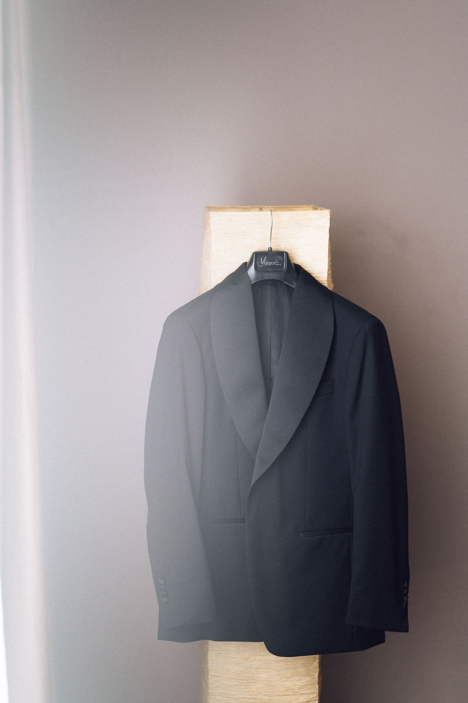 Black tuxedo jacket hanging on a wooden stand against a gray wall, perfect for formal events.