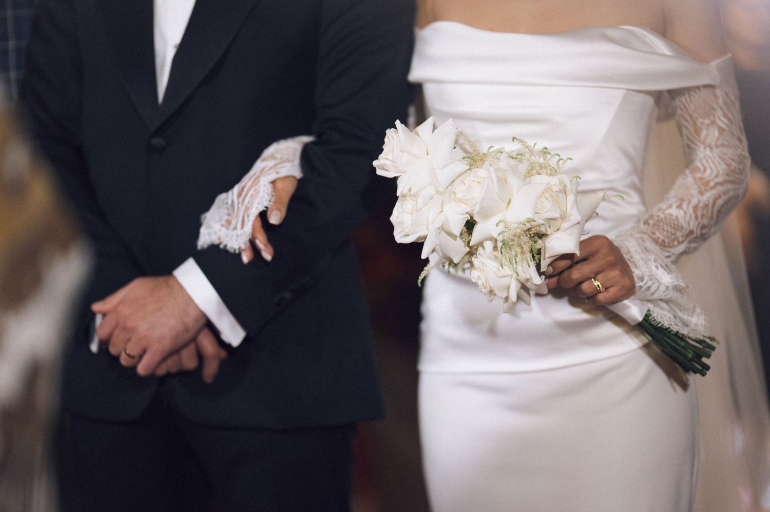 Bride holding white floral bouquet beside groom in black tuxedo during elegant wedding ceremony.