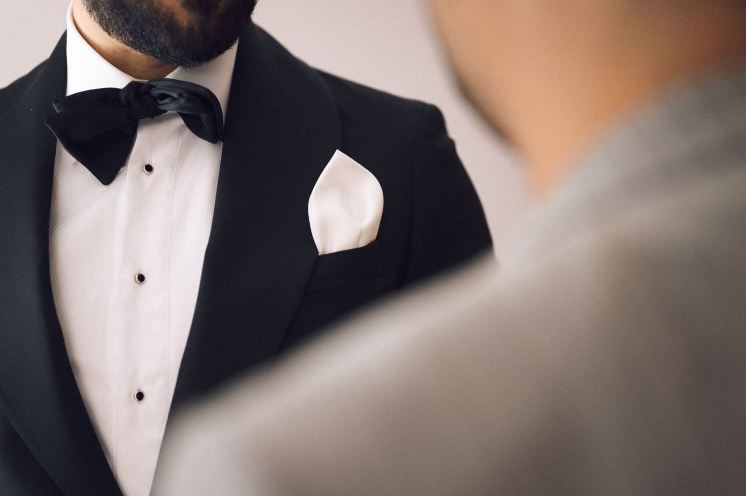 Man in black tuxedo with bow tie and white pocket square, elegant formal attire for wedding or black tie event.