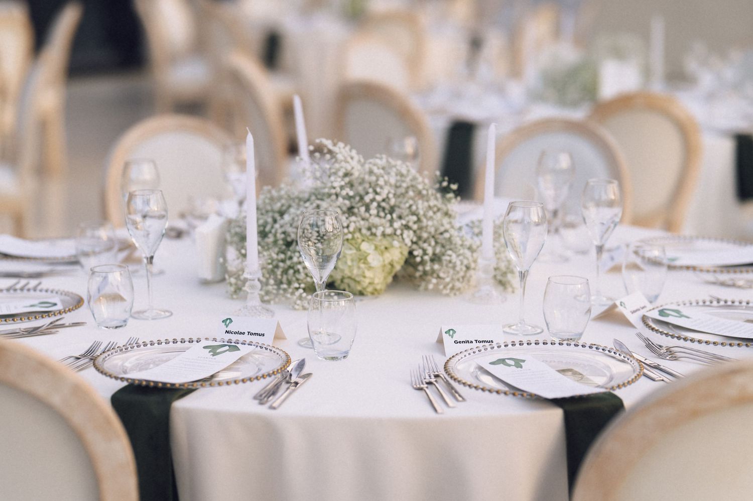 Elegant wedding reception table set with white linens, crystal glasses, silver charger plates, and baby's breath floral centerpiece.