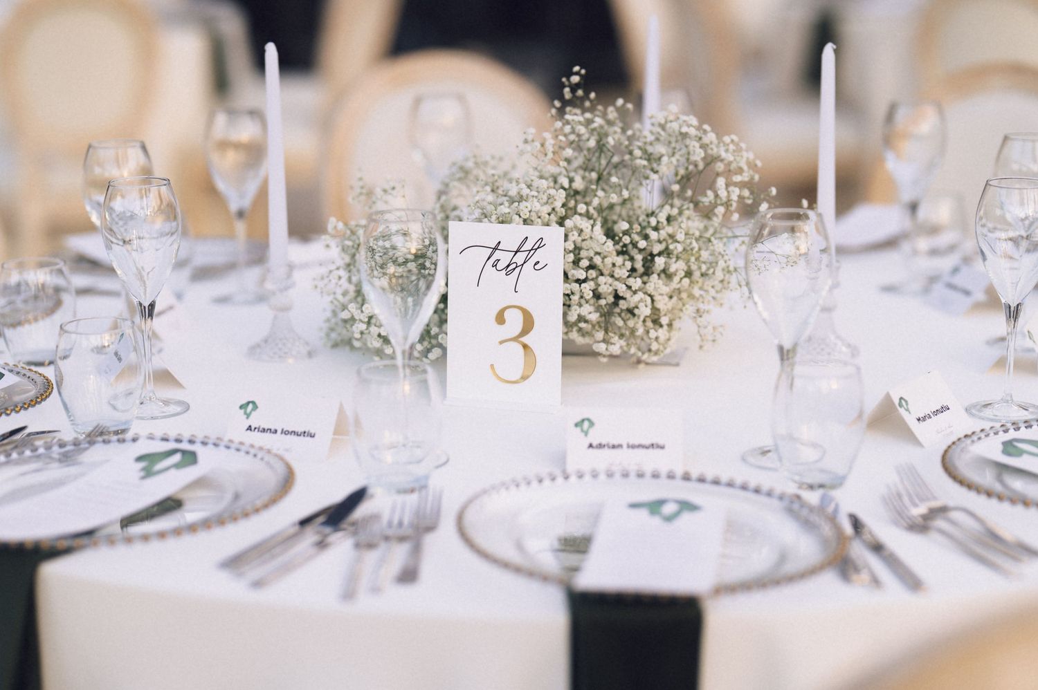 Elegant wedding reception table setting with baby's breath centerpiece, white candles, and crystal glassware on white linen.