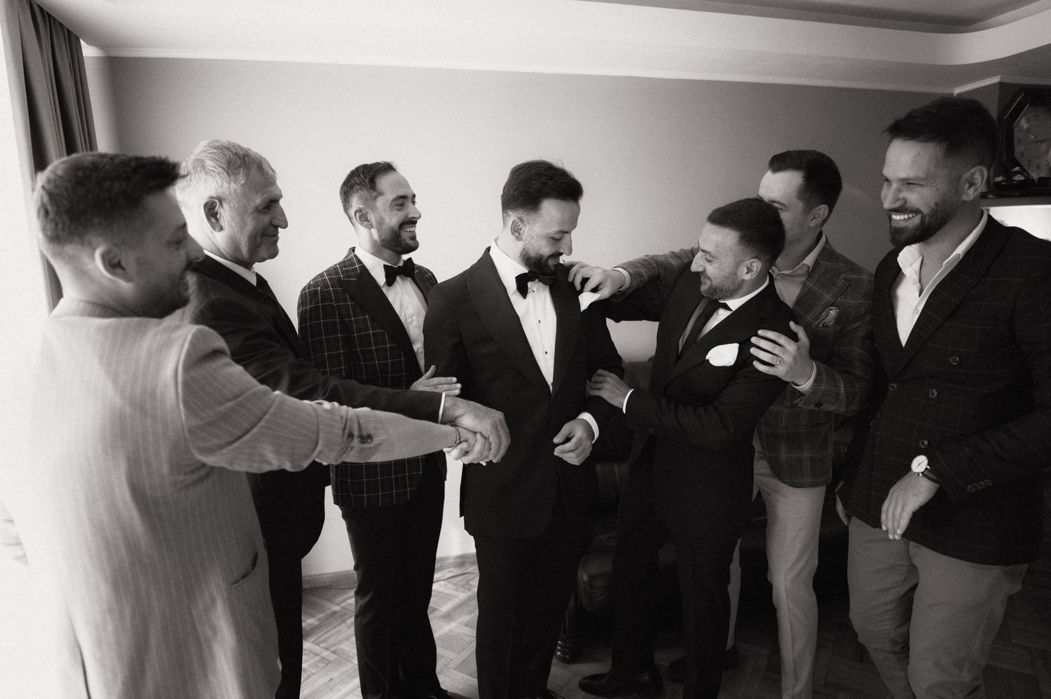 Black and white photo of groom and groomsmen laughing together before wedding ceremony.