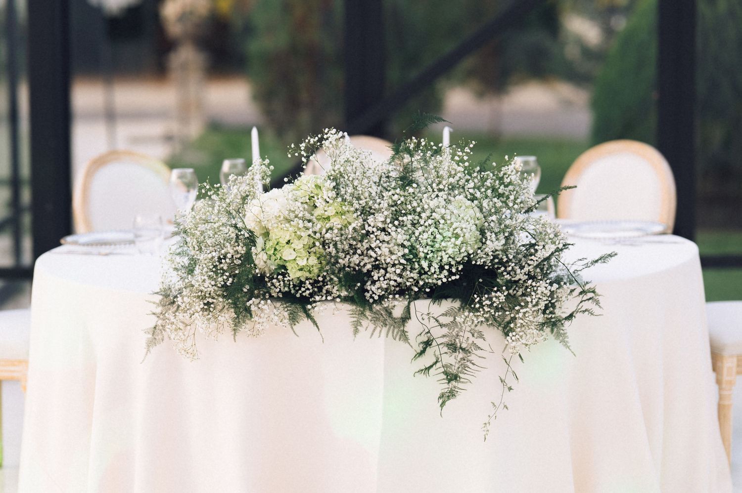 Elegant wedding sweetheart table with white linen and lush baby's breath and greenery floral centerpiece.