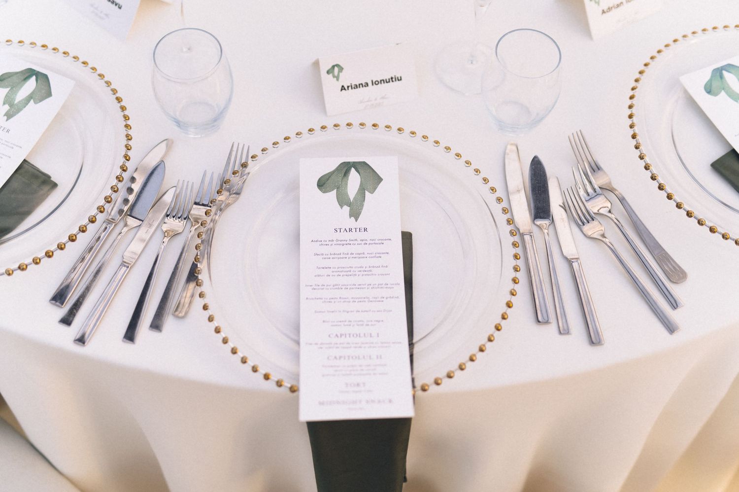 Elegant wedding table setting with gold beaded charger plates, silver cutlery, crystal glasses, and a floral menu card.