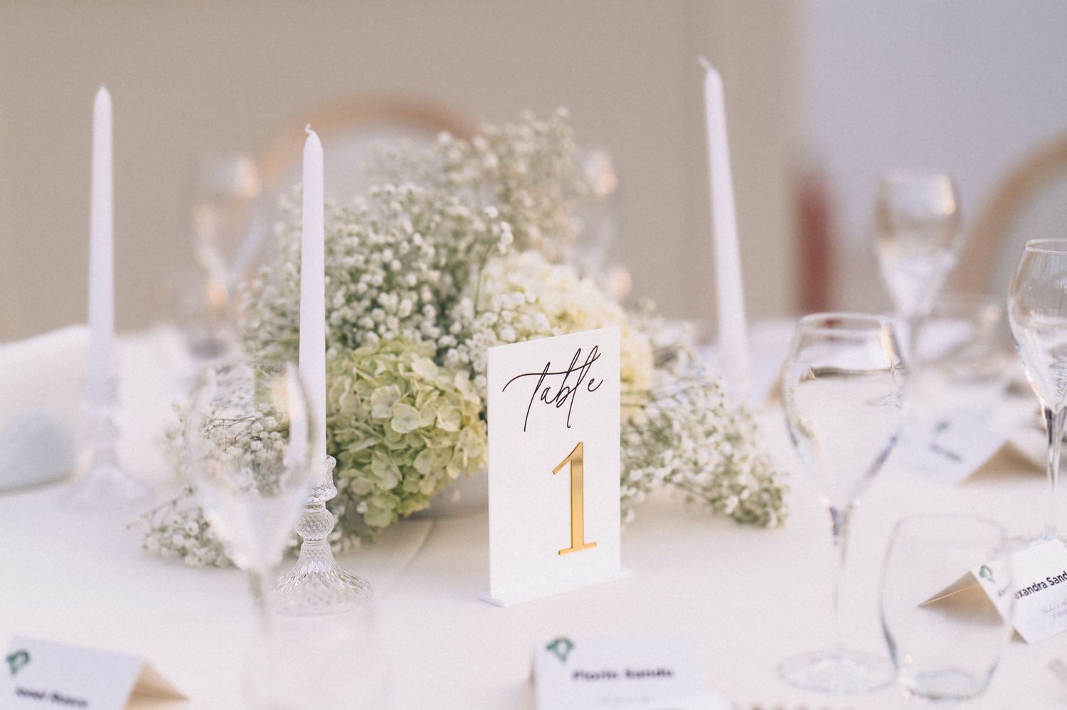 Elegant wedding table setting with white floral centerpiece, candles, and a gold Table 1 number card.
